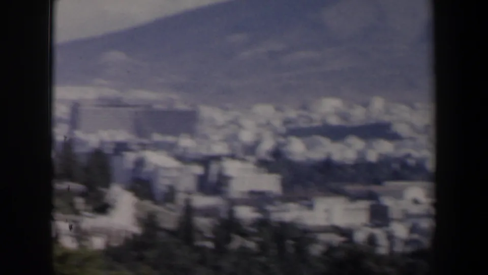 1960 8mm view in Israel of a large city spreading below mountains, with soft focus and trees at the edge.
