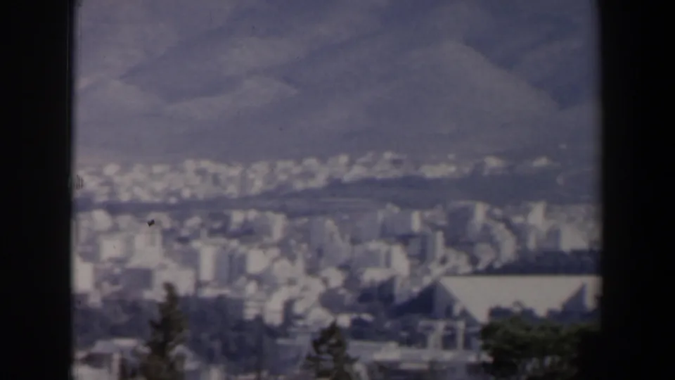 Soft 8mm frame from Israel in 1960 showing dense urban buildings, trees, and a mountain backdrop.