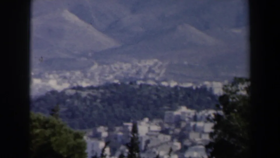 1960 8mm Israel travel frame showing trees in the foreground, a distant settlement in a valley, and hazy mountains beyond.