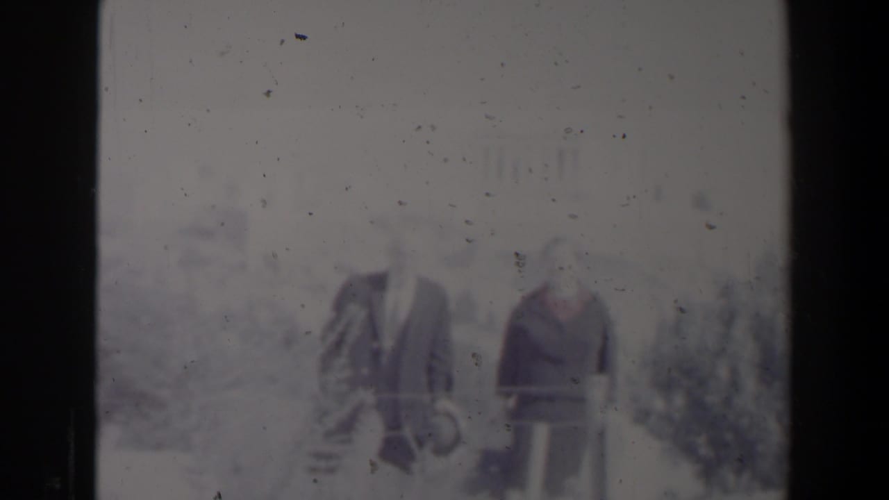 Two adults continue walking outdoors in a faded, soft-focus 8mm frame.