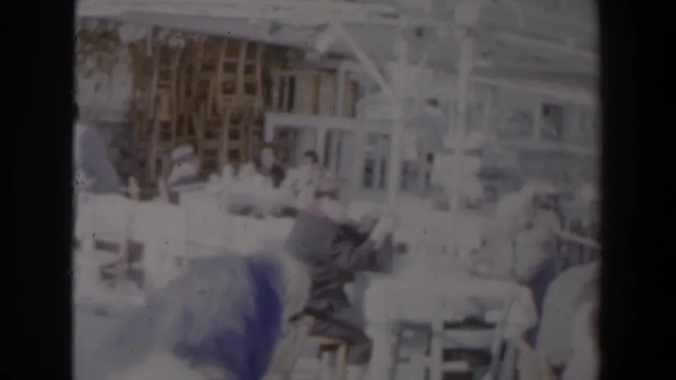 1960 Israel factory scene with women working at sewing machines amid tables, fabric, shelving, and overhead structure.