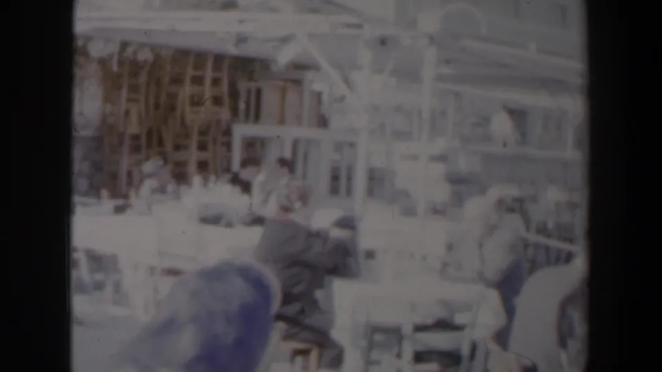 Overexposed 1960 Israel home-movie frame showing an outdoor restaurant table with seated figures near a waterfront area.