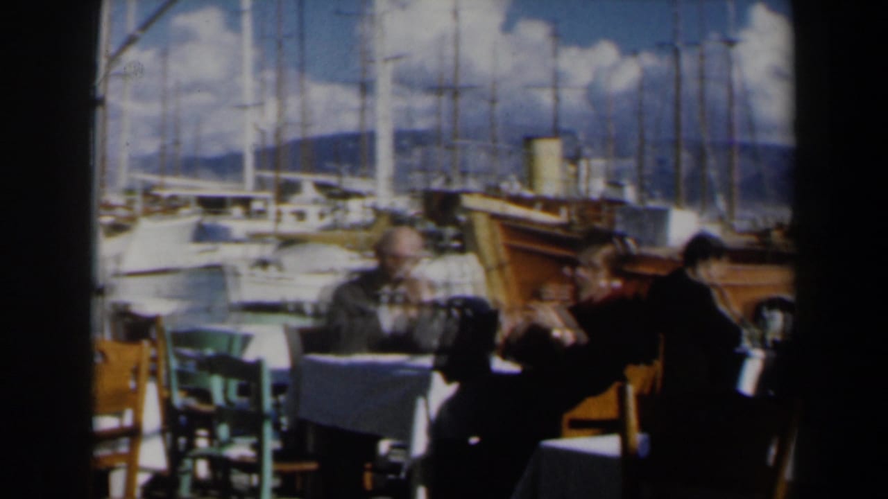 Restaurant patrons sit at tables near docked boats and tall sailboat masts.