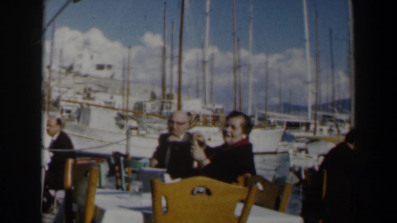 Adults seated at outdoor cafe tables beside a yacht harbor.