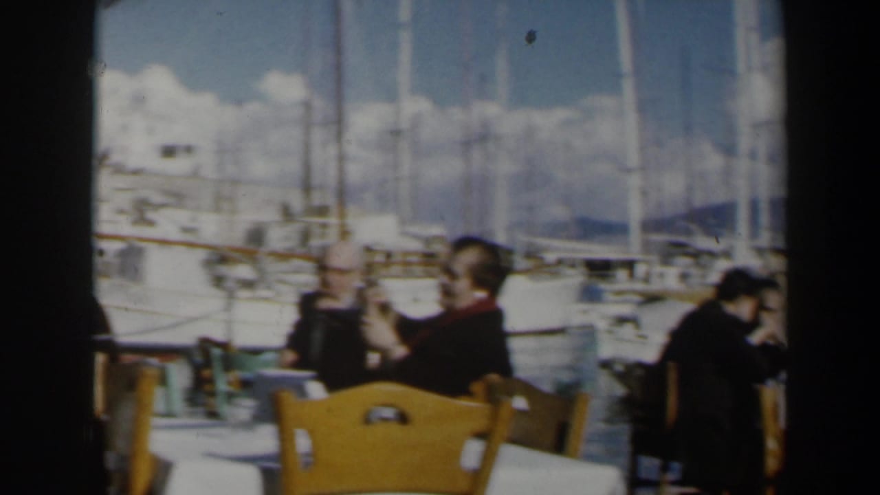 Adults in period attire sit at a sunny harbor cafe in Israel, with yachts and masts filling the background.