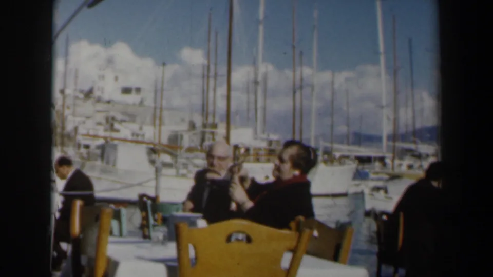 A 1960 Israel vacation frame shows cafe seating, adult patrons, and a marina backdrop with boats and masts.