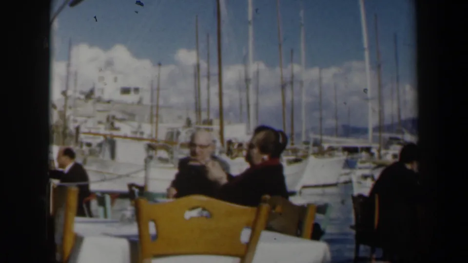 Final frame of a short 1960 Israel harbor cafe scene, with seated adults and moored yachts in soft 8mm color.