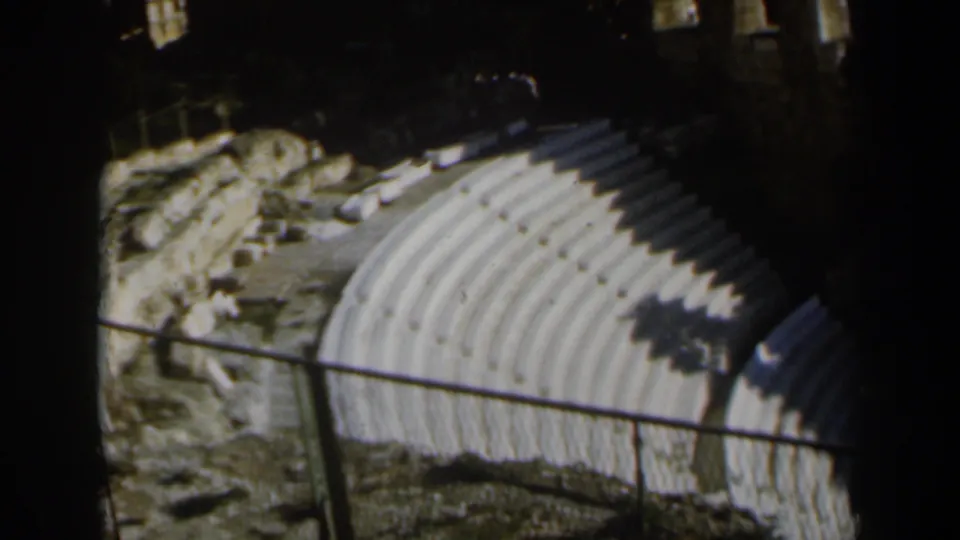 Visitor-shot 1960s Israel view of ancient-style stone amphitheater seating, ruins, and railings in strong shadow.