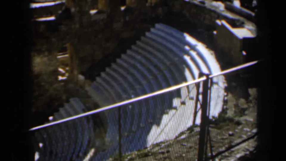 Handheld 8mm frame of tiered stone seating, railings, broken masonry, and shadowed ruin walls in Israel, 1960.