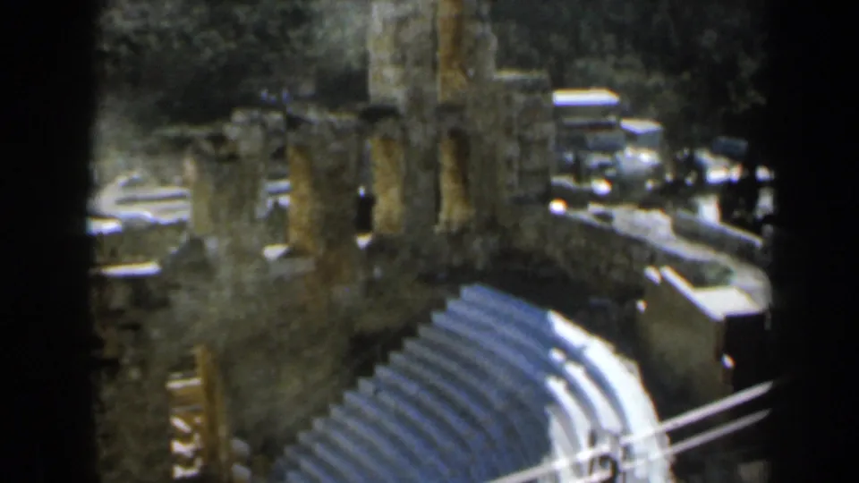 1960 8mm view in Israel looking down over tiered stone amphitheater seating, ruined columns, and a wooded hillside.
