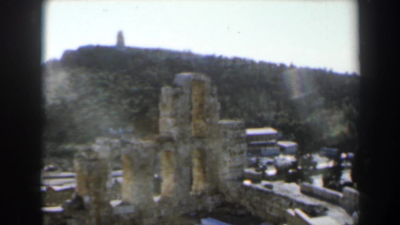 Ruined stone structure and path below a wooded hill with a distant monument.