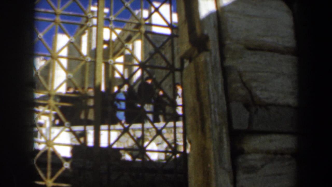 Iron gate and stone structure with distant visitors in shadow.