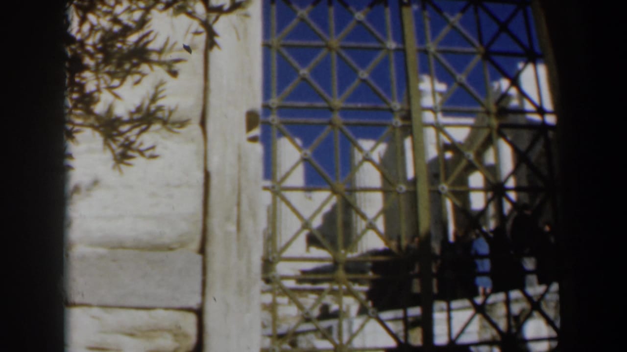 View through a tan iron gate beside pale stonework and tree branches.