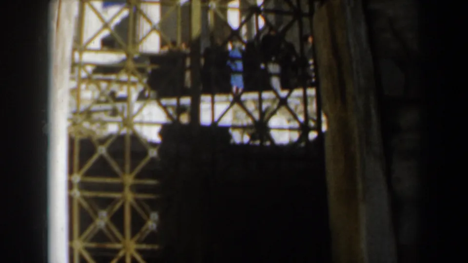 Decorative iron gate in a shaded foreground, with pale stone surfaces and bright blue sky visible beyond in the 1960 Israel home movie.