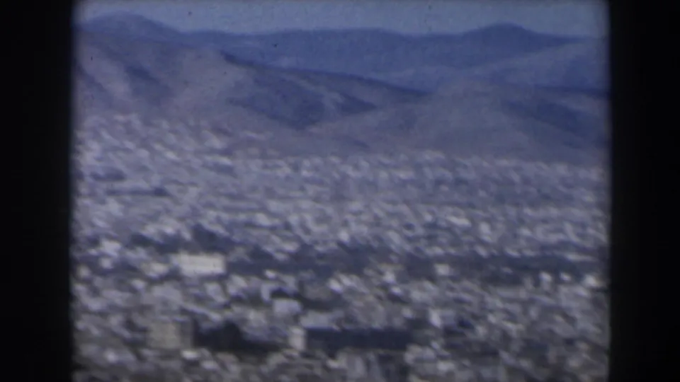 1960 Israel 8mm frame showing a hazy aerial cityscape below distant rugged mountains, seen through dark viewer borders.