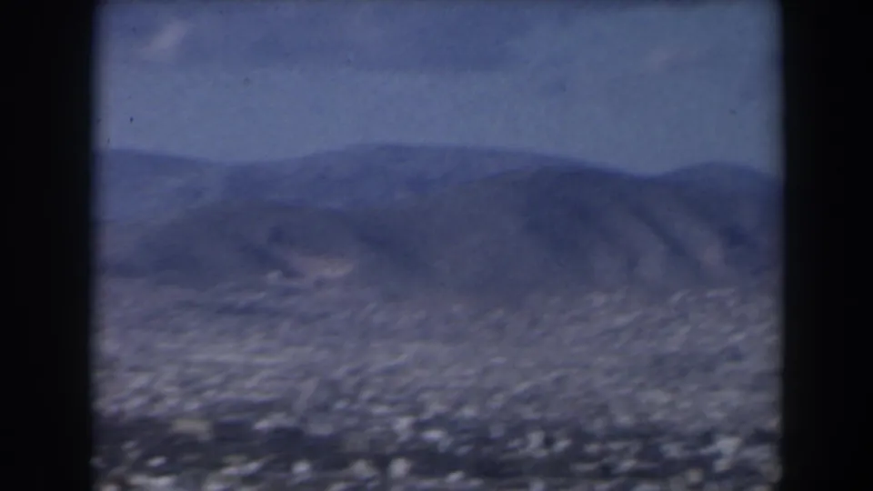 1960 Israel 8mm frame with a broad urban area below a blue-gray mountain ridge and visible dark scan borders.