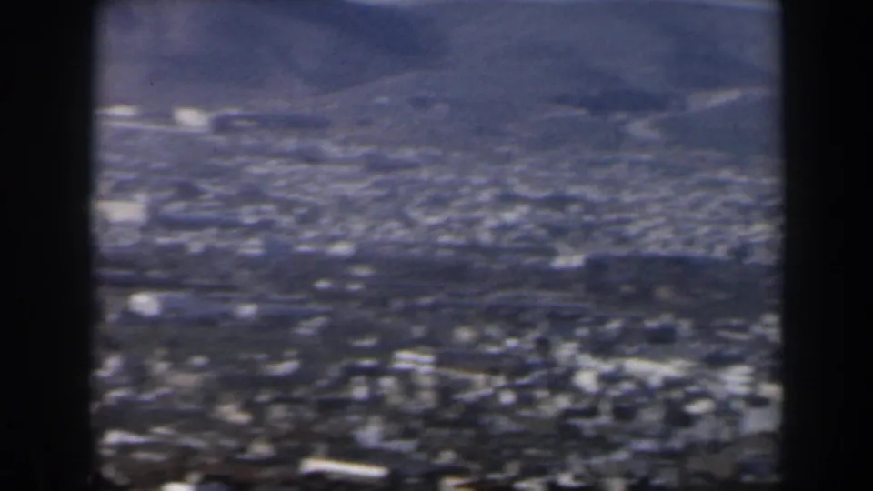 1960 Israel 8mm frame showing a hazy urban basin with mountains beyond, bordered by dark film or viewer edges.