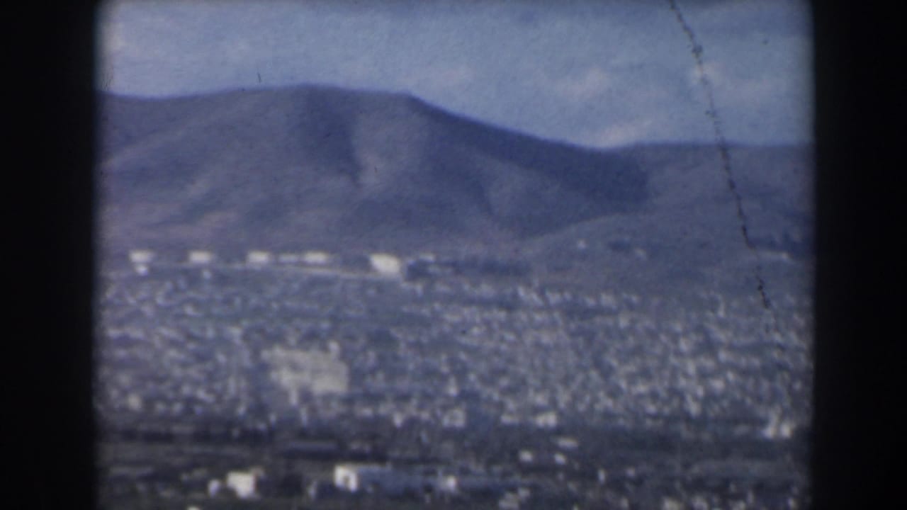1960 Israel home-movie frame showing a distant city in a valley with hazy hills and mountains beyond.