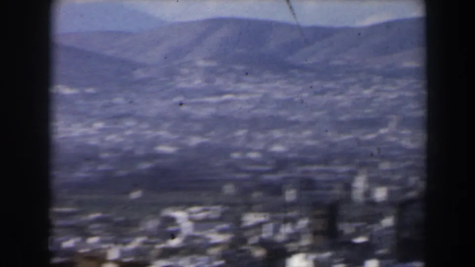 Faded 8mm frame from 1960 Israel showing a hazy valley city and rolling hills from an elevated viewpoint.