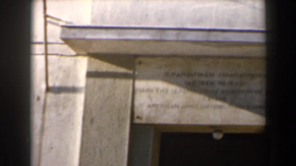 1960 Israel 8mm frame showing a weathered Greek and English plaque above a shaded building entrance.