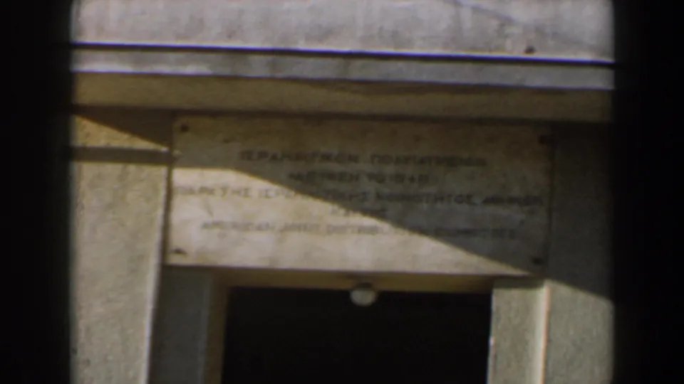 1960 Israel 8mm frame showing a weathered stone donation plaque above a recessed doorway, partly crossed by sunlight and shadow.