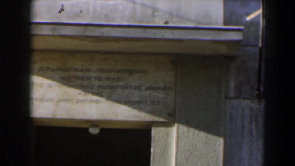 Final 8mm frame of the Israel plaque shot, showing the weathered inscription panel, entrance shadow, and small lamp beneath it.