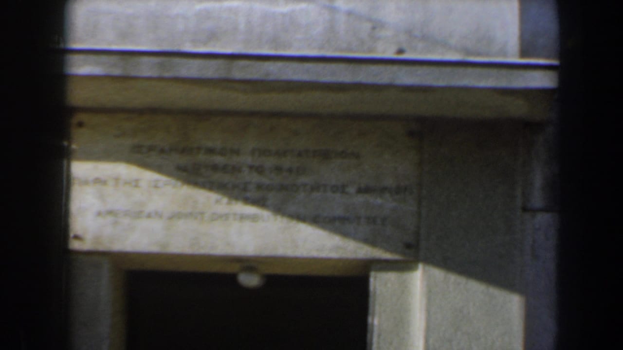 Stone plaque above a dark doorway, partly obscured by foreground vertical bars.