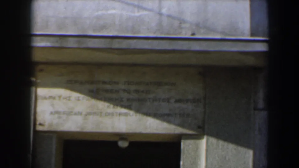 1960 Israel 8mm frame with a faded bilingual stone inscription above a dark recessed entrance.