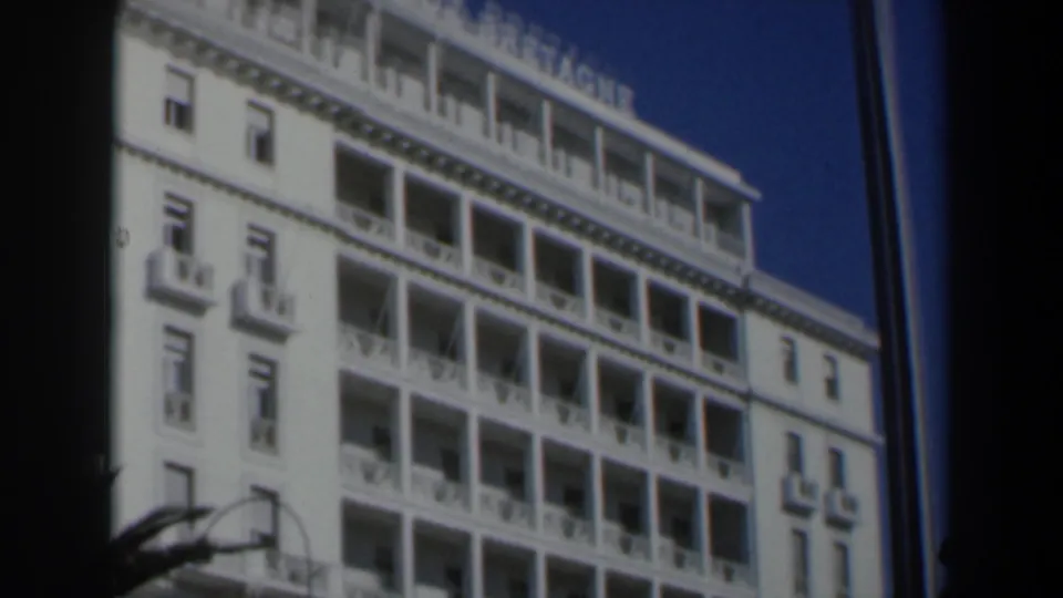 1960 Israel 8mm view of the upper hotel facade, showing stacked balconies, windows, blue sky, and dark film borders.