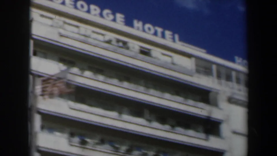 1960 Israel 8mm close view of upper hotel balconies with partial rooftop hotel lettering visible against blue sky.