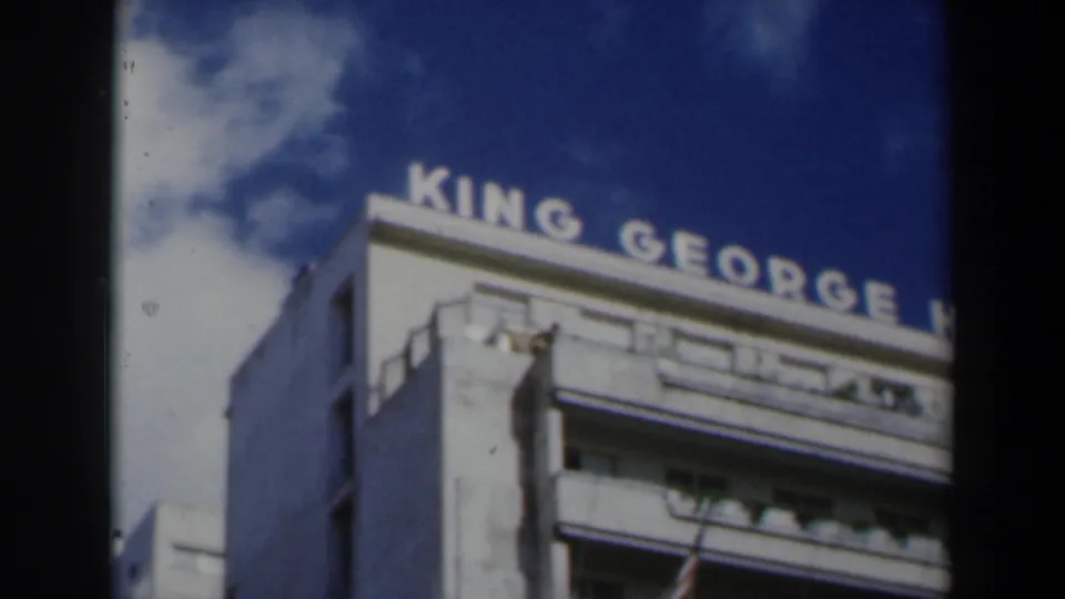 1960 Israel travel frame with the King George Hotel rooftop letters partly cropped above a white multi-story facade and cloudy blue sky.