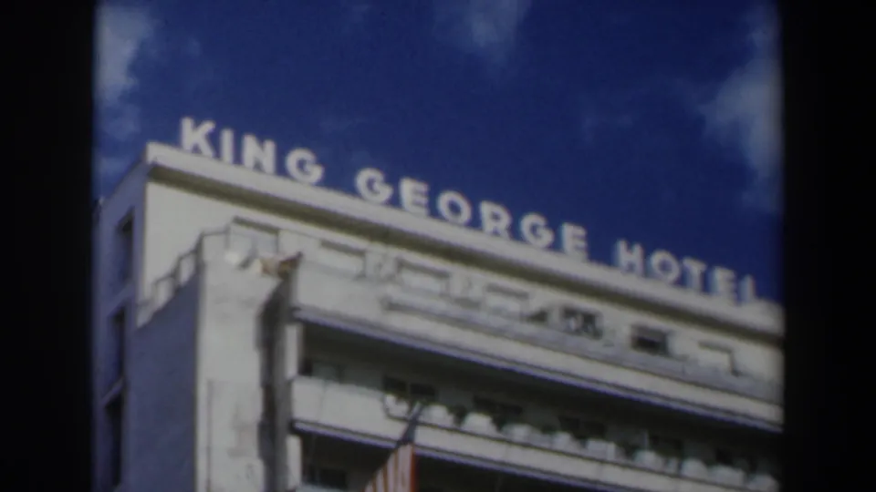 1960 Israel 8mm frame showing the King George Hotel sign across the roofline, white exterior balconies, blue sky, and a flag hanging below.