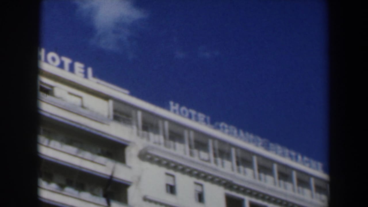 1960 Israel 8mm frame showing the upper facade of Hotel Grande Bretagne with partial rooftop signage and deep blue sky.