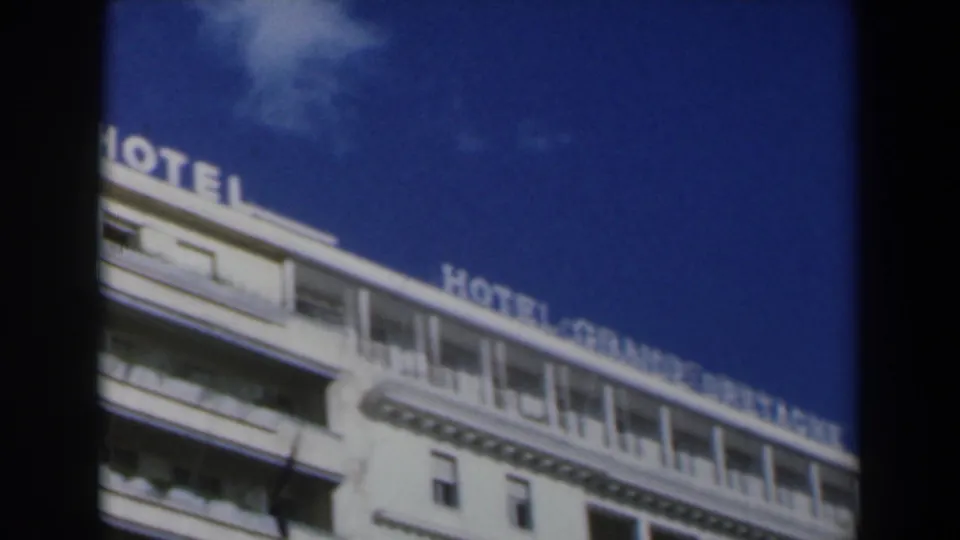 1960 Israel 8mm frame showing the upper facade of Hotel Grande Bretagne with partial rooftop signage and deep blue sky.