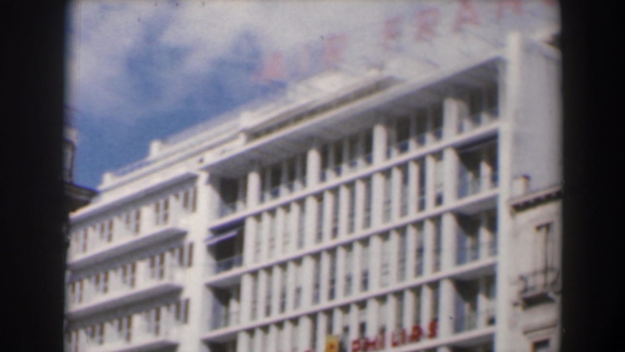 1960s Israel frame of a white modernist building with balconies, vertical window bays, and visible commercial signage.