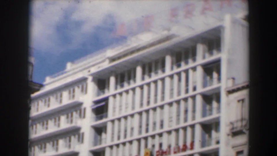 1960s Israel frame of a white modernist building with balconies, vertical window bays, and visible commercial signage.