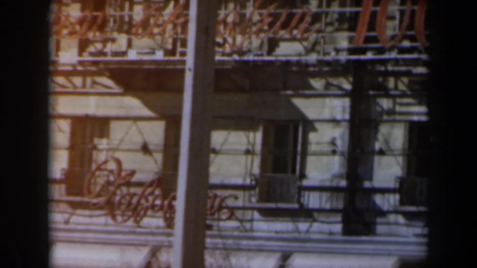 Urban facade in Israel with balconies, awnings, street poles, and partial commercial signage on 8mm film.