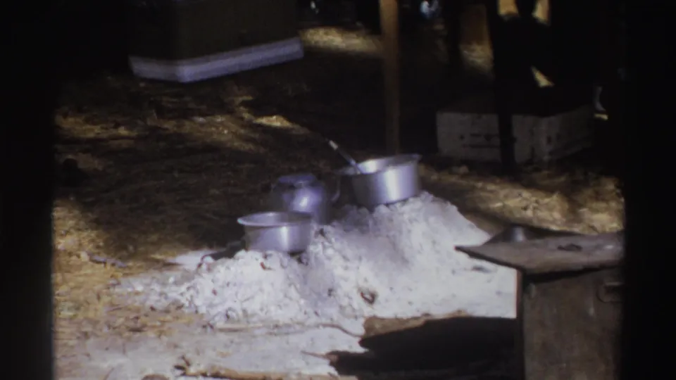 1969 South Africa campsite frame with metal pots set beside a pale ash or sand pile inside or near a tent opening.