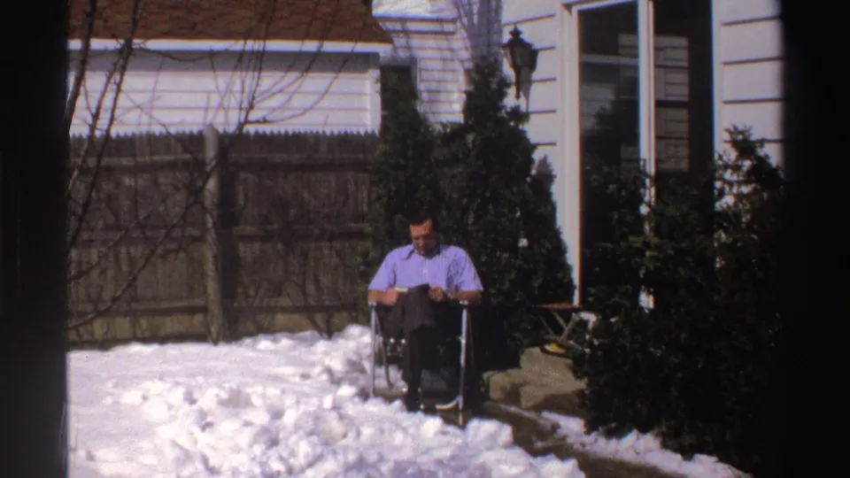 Near the end of the 1969 Michigan clip, the seated man looks down while surrounded by deep backyard snow.