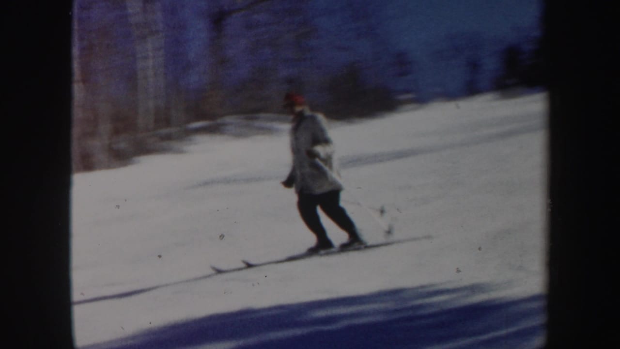 Skier in a light coat gliding across snow with poles.