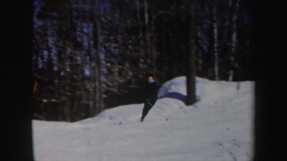 1962 Vermont frame showing a dark-clothed skier near a snowbank and tree line on a winter slope.
