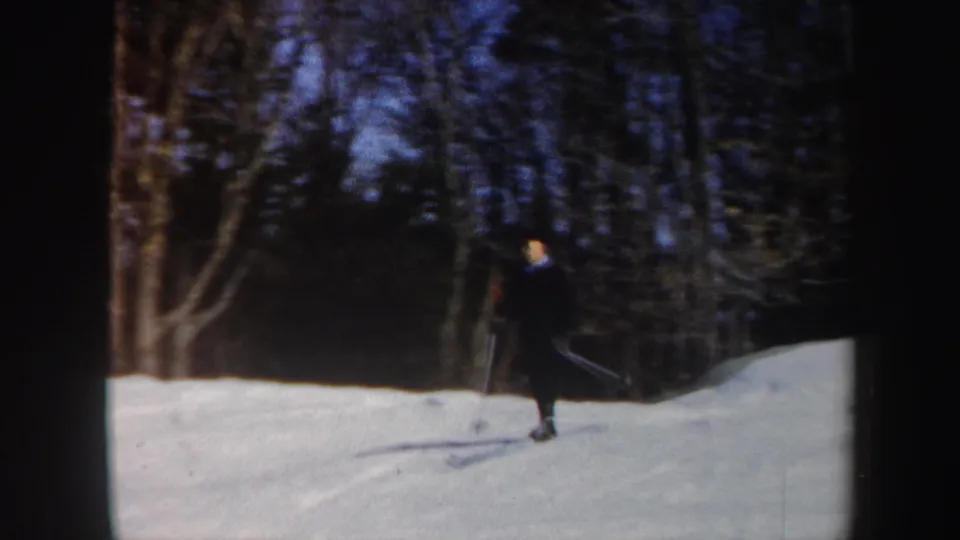 Adult man in a dark suit and hat skis on a snowy Vermont slope in 1962 home-movie footage.