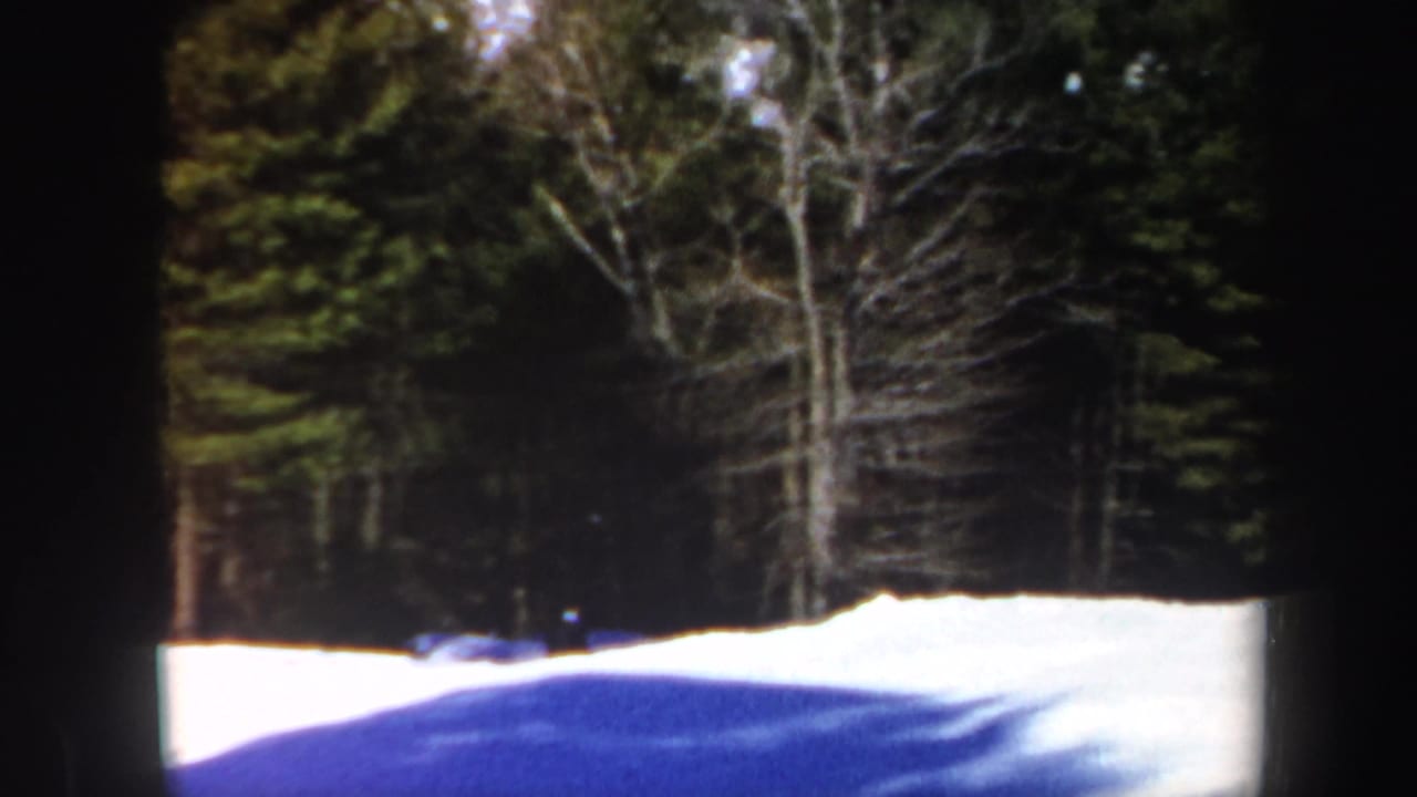 1962 Vermont frame with a snow-covered ski slope, dense winter trees, and a small dark skier near the edge of the woods.