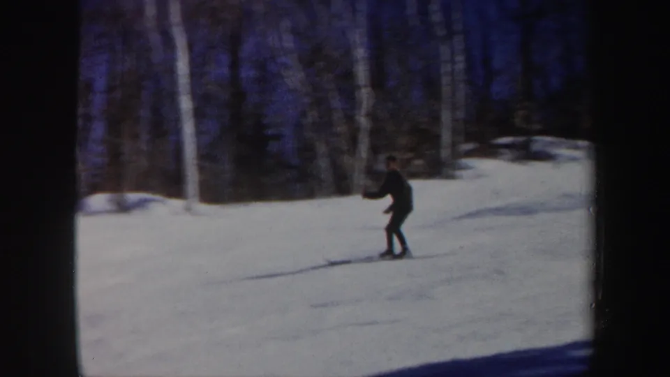 The skier continues downhill through snow in a wooded Vermont setting, with leafless trees and soft 8mm color visible.