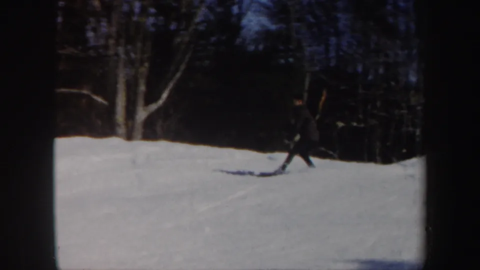 A lone skier in Vermont, 1962, moves across a snow-covered hillside with leafless trees in the background.