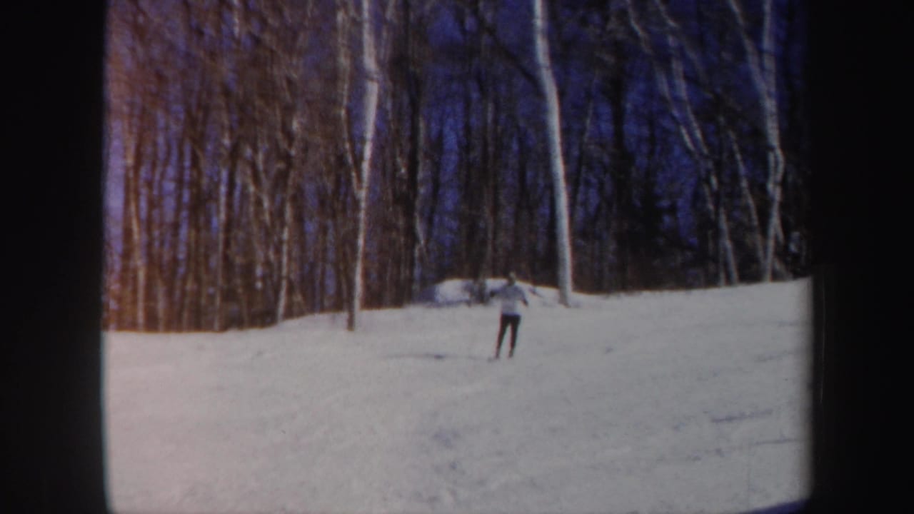 A single skier descends a Vermont snow slope in 1962, framed small against woods and blue winter sky.