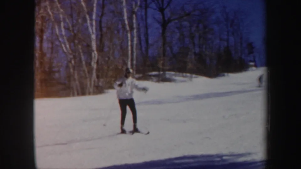 A lone skier nears the camera on a Vermont snow slope, with long shadows and wooded background visible in the 1962 footage.