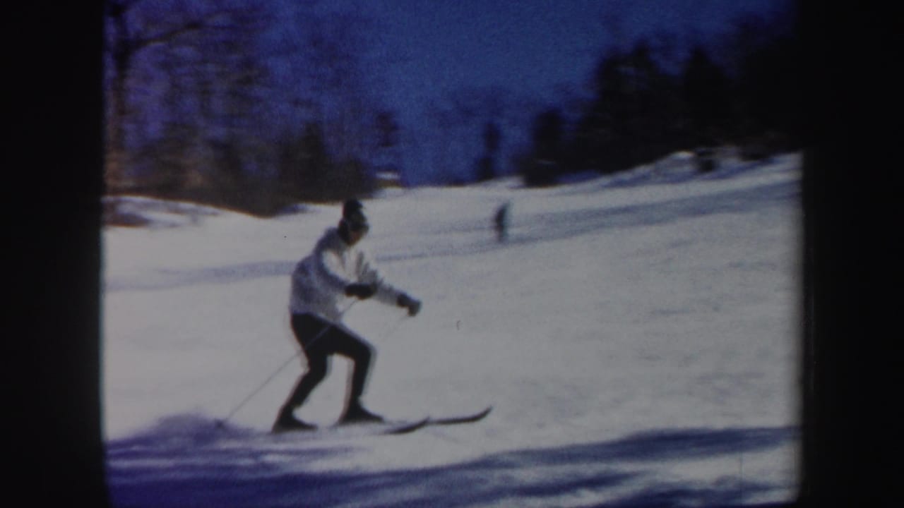 A skier in a white jacket and dark pants glides across a snowy Vermont slope in 1962 home-movie footage.