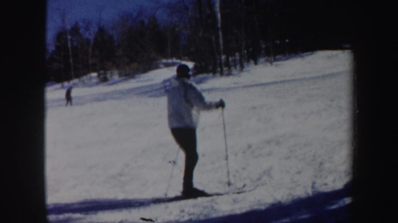 Skier stands or slows on the snowy slope with poles planted.