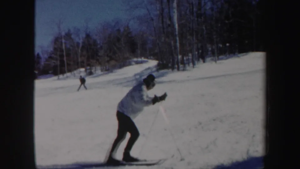 A skier in a white jacket leans forward with poles while crossing a snowy Vermont slope in 1962.